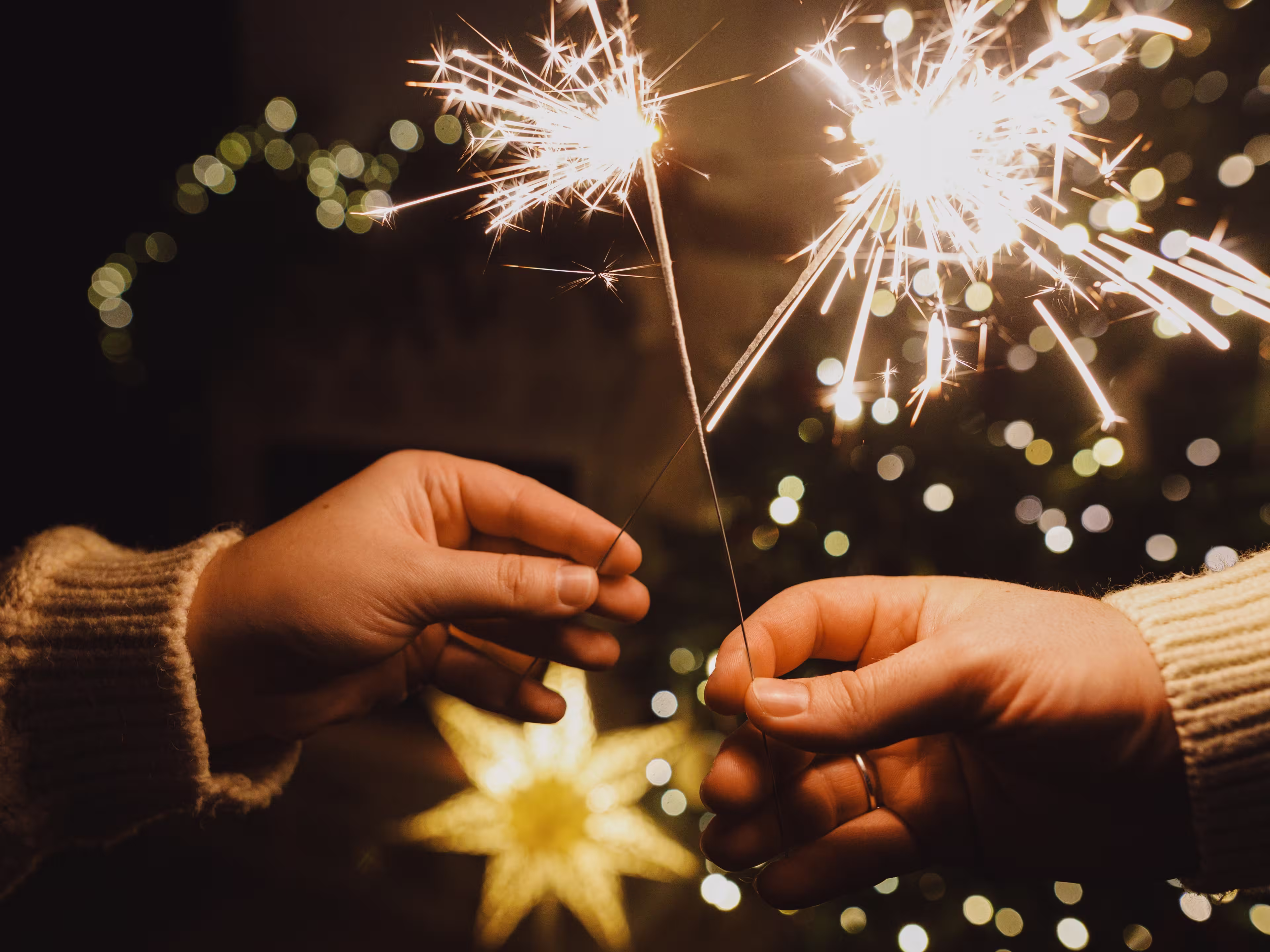 Happy New Year! Burning sparklers in hands on background of christmas tree golden lights bokeh at night. Glowing fireworks in couple hands, new year eve holiday celebration