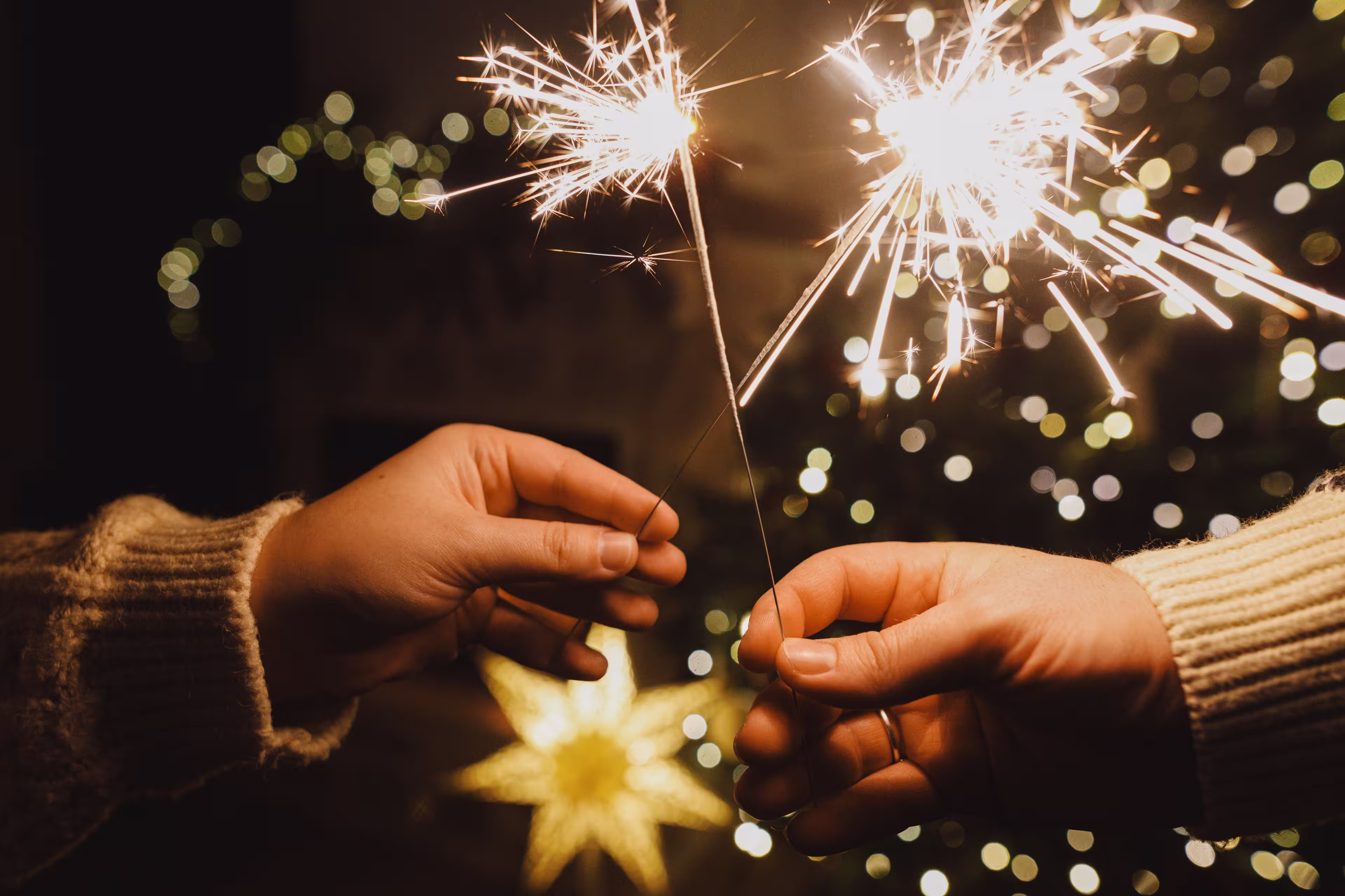 Happy New Year! Burning sparklers in hands on background of christmas tree golden lights bokeh at night. Glowing fireworks in couple hands, new year eve holiday celebration
