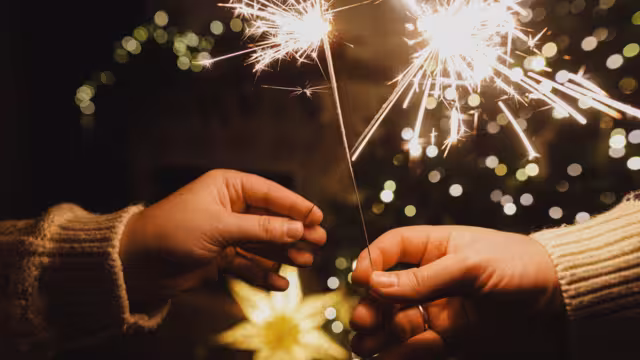 Happy New Year! Burning sparklers in hands on background of christmas tree golden lights bokeh at night. Glowing fireworks in couple hands, new year eve holiday celebration