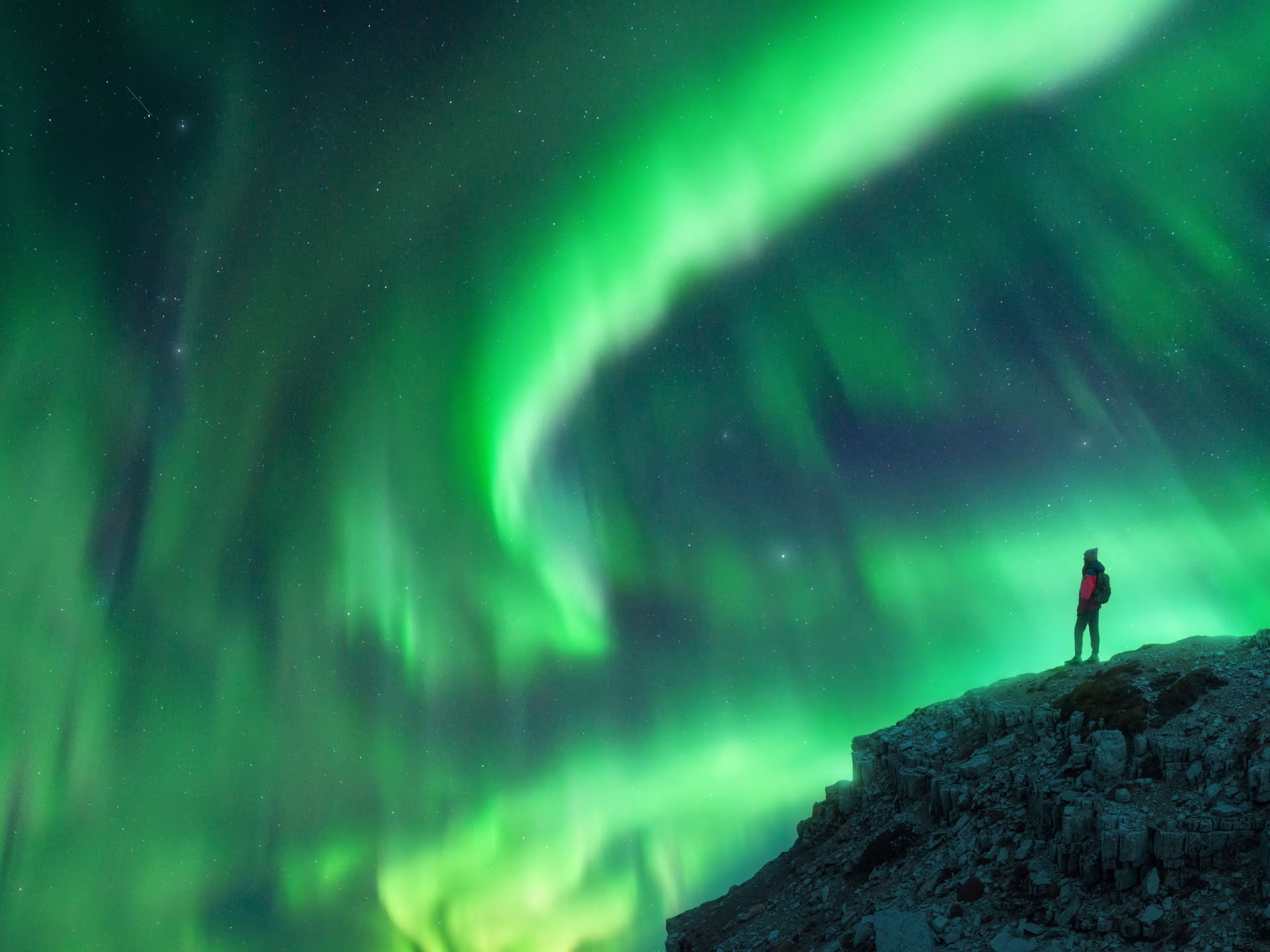 Northern lights and young woman on mountain peak at night. Aurora borealis and silhouette of alone girl on top of rock. Landscape with polar lights. Starry sky with bright aurora. Travel background