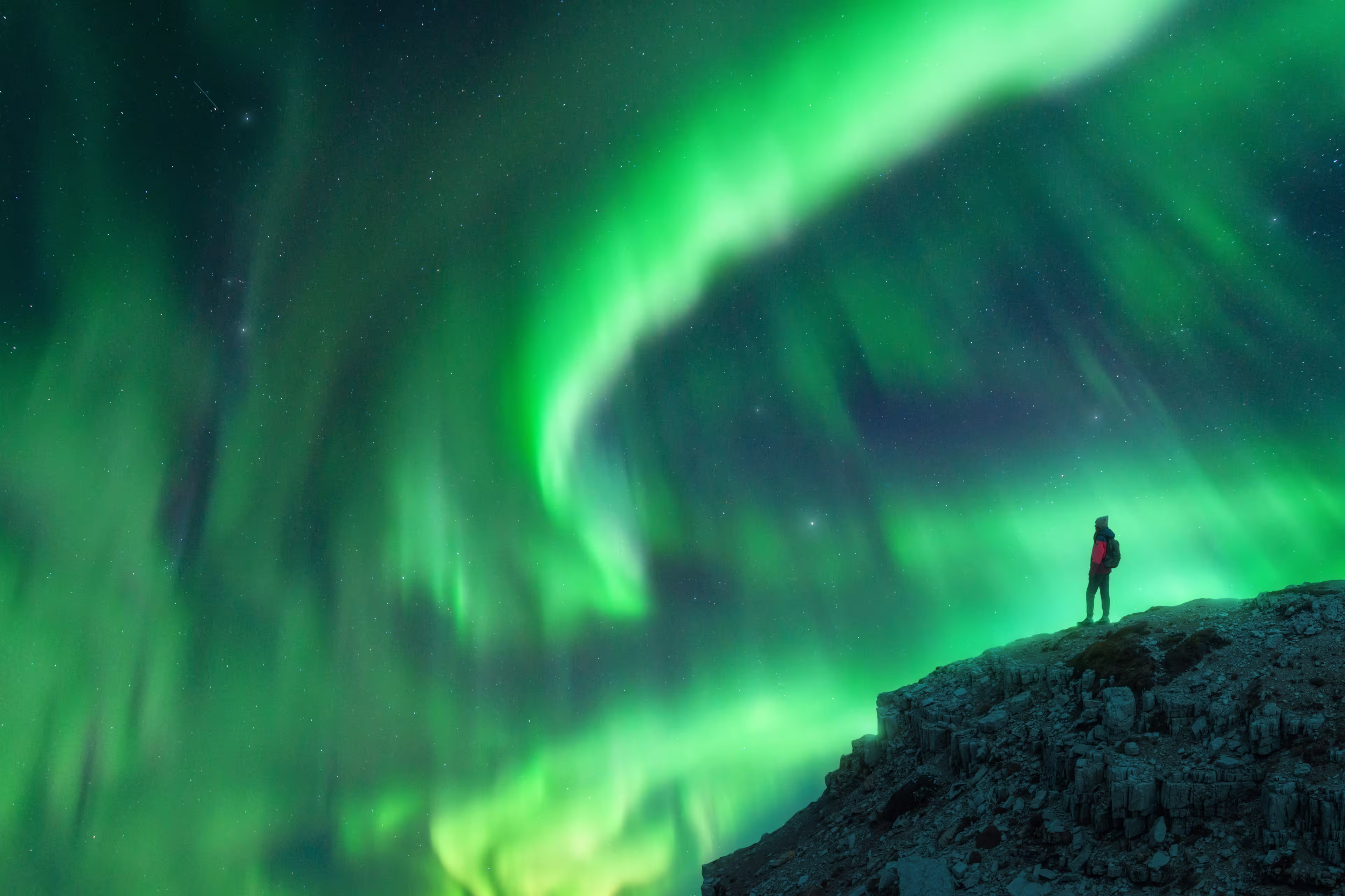 Northern lights and young woman on mountain peak at night. Aurora borealis and silhouette of alone girl on top of rock. Landscape with polar lights. Starry sky with bright aurora. Travel background