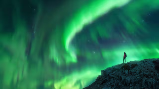Northern lights and young woman on mountain peak at night. Aurora borealis and silhouette of alone girl on top of rock. Landscape with polar lights. Starry sky with bright aurora. Travel background