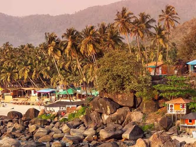 Tropical sunset beach with bungalow and coconut palm trees at Palolem in Goa, India