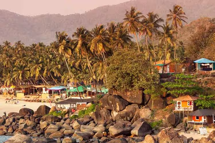 Tropical sunset beach with bungalow and coconut palm trees at Palolem in Goa, India