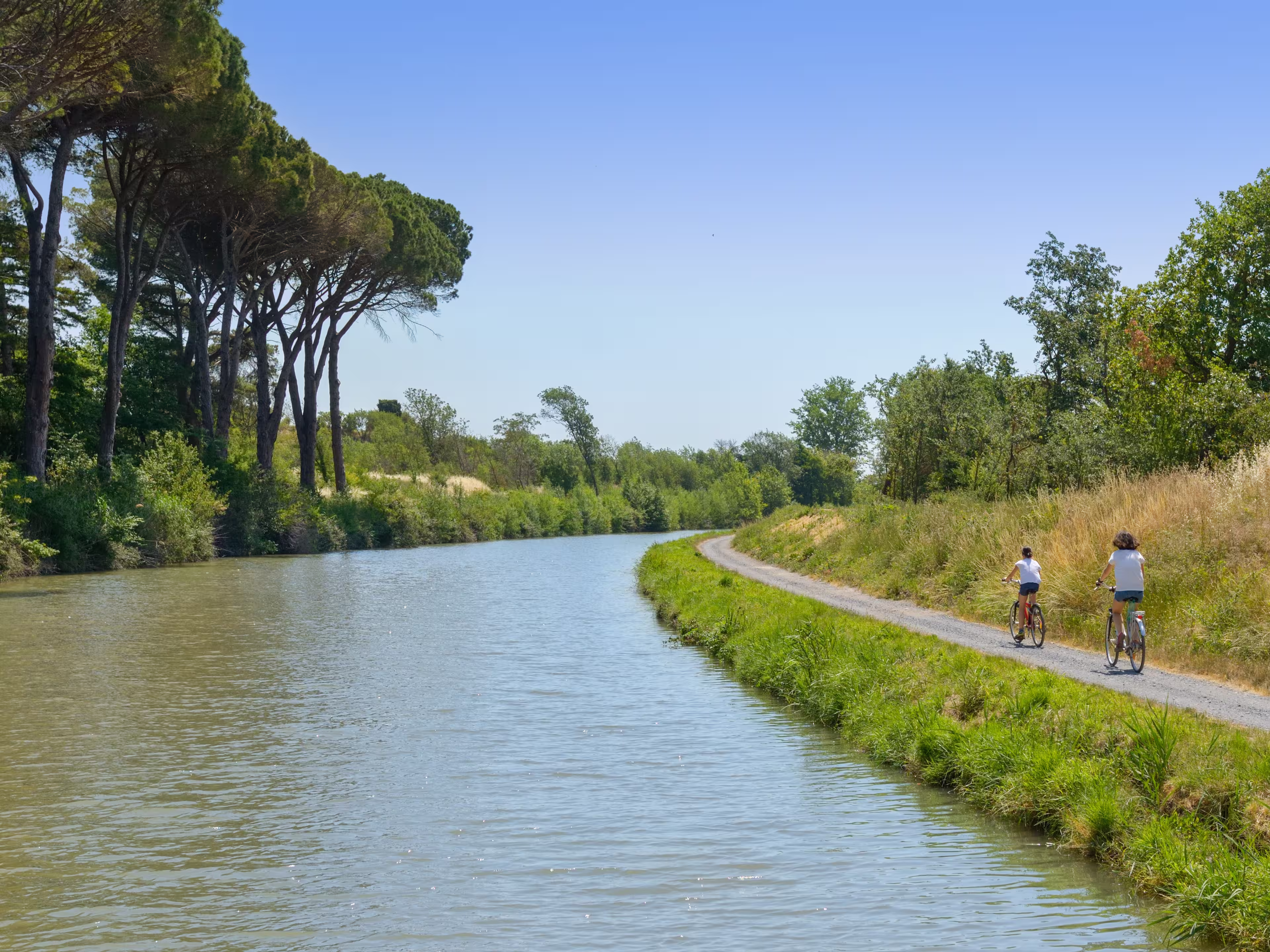 Family on bikes, mother and daughter cycling by canal du Midi, active summer vacation in France