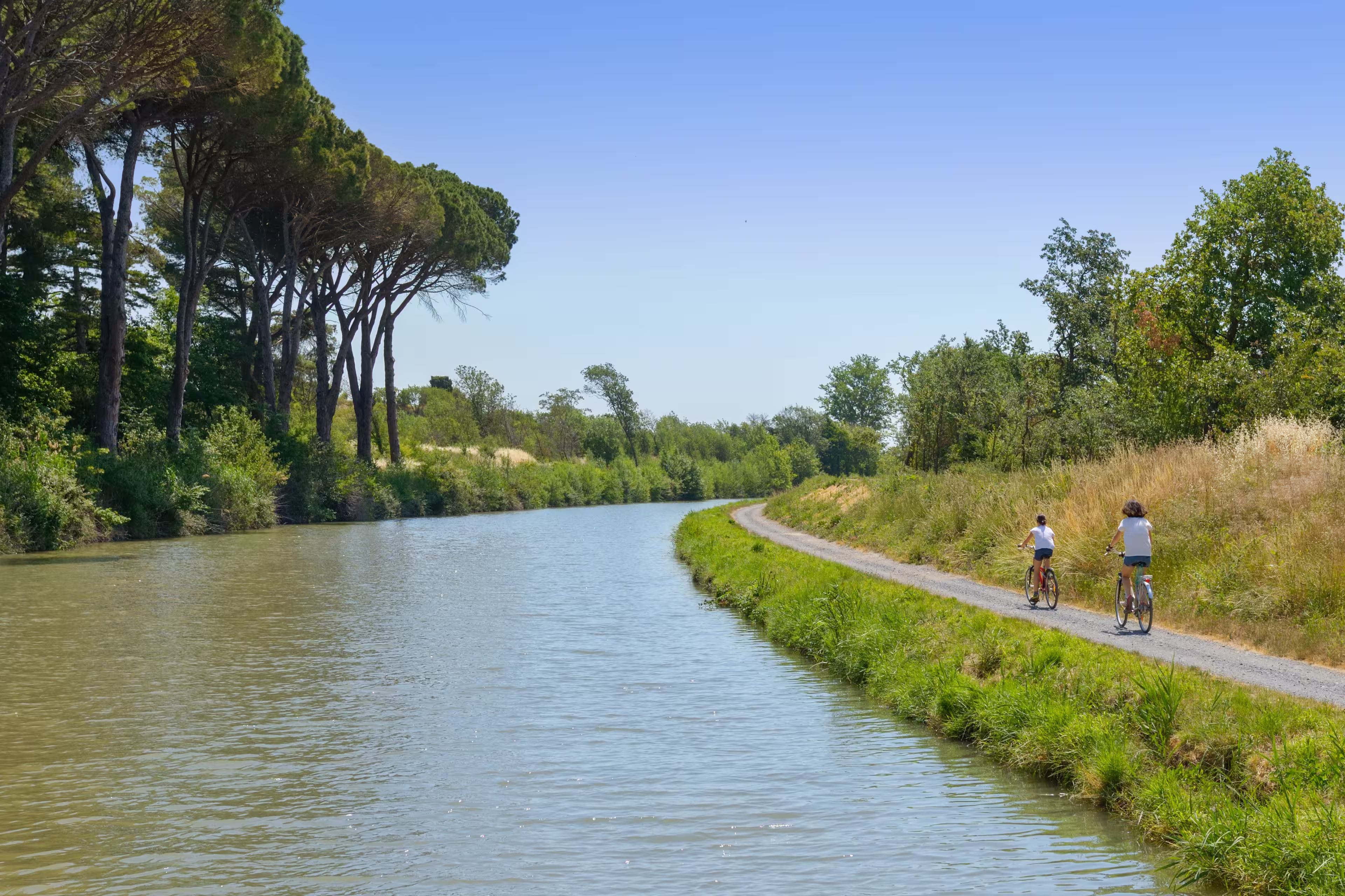 Family on bikes, mother and daughter cycling by canal du Midi, active summer vacation in France
