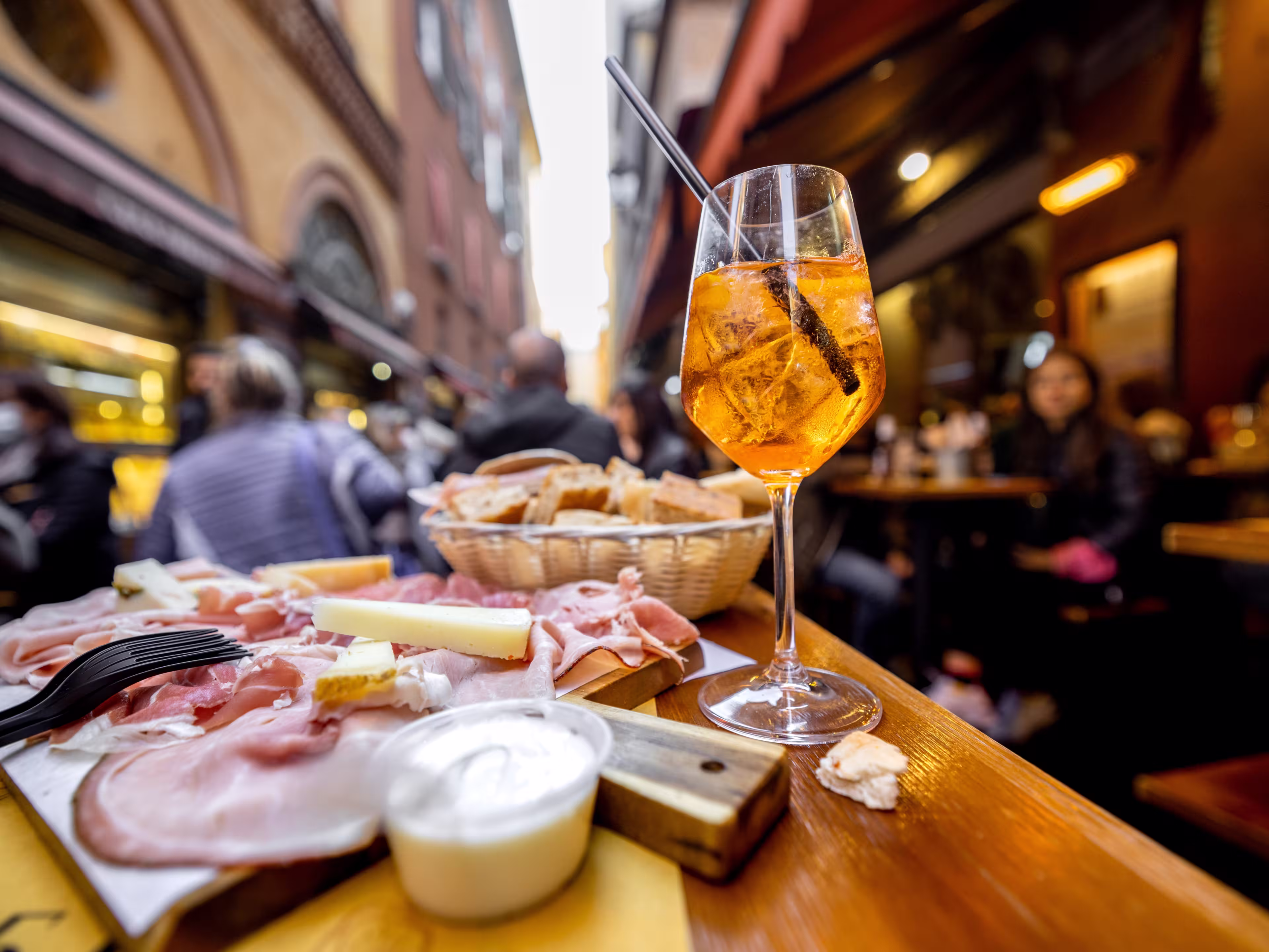 Meat plate with sliced italian sausages, proscutto, cheese, bread and Spritz Aperol drink on a table at outdoor bar on crowded street background