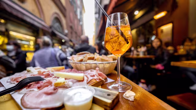 Meat plate with sliced italian sausages, proscutto, cheese, bread and Spritz Aperol drink on a table at outdoor bar on crowded street background
