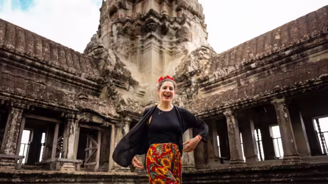Traveller smiling in front of one of the corners of Angkor Wat, showing the intricate architecture, Siem Reap, Cambodia