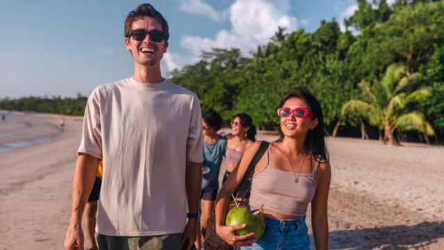 Young Intrepid travellers stroll along a beach in the Philippines with drinking coconuts laughing and enjoyng the sun